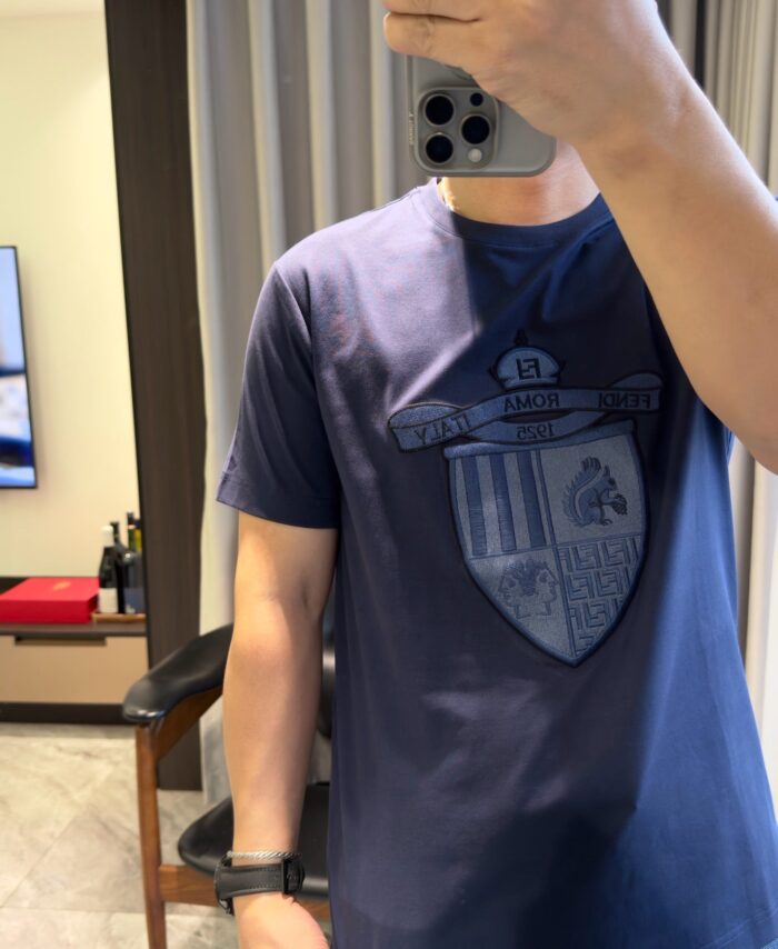 Selfie casual in casa con maglietta blu con logo a scudo e ambiente moderno e accogliente.