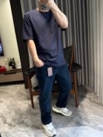 Elegante look casual con T-shirt navy, jeans scuri e sneakers bianche in ambiente moderno.
