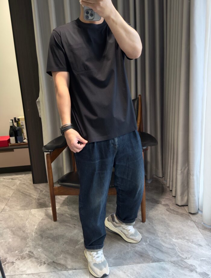 Persona con t-shirt nera, jeans larghi e sneakers in ambientazione moderna e accogliente.