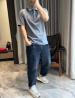 Persona in outfit casual con polo grigia, jeans larghi e sneakers bianche in ambientazione moderna.