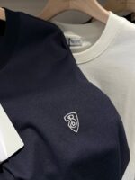 Magliette casual navy blu e bianco su grucce in legno, logo ricamato e design semplice.