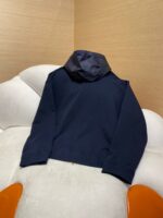 Giaccone navy con cappuccio e design minimalista su divano beige, stile elegante e casual.