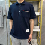 Uomo in polo navy con taschino a strisce rosse e bianche, joggers grigi, stile casual moderno.