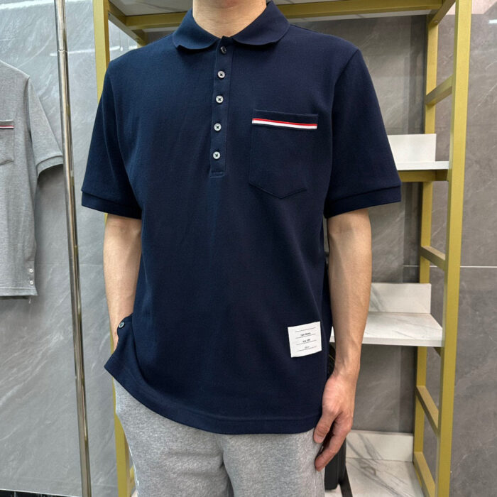 Uomo in polo navy con taschino a strisce rosse e bianche, joggers grigi, stile casual moderno.