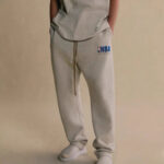 Pantaloni jogger grigi con logo NBA e sneakers bianche, stile casual sportivo.