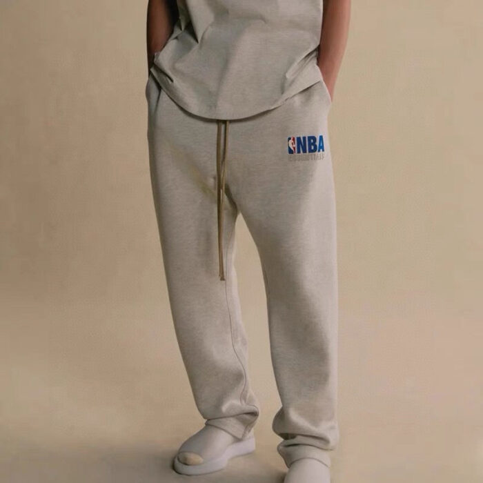 Pantaloni jogger grigi con logo NBA e sneakers bianche, stile casual sportivo.