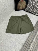 Pantaloncini casual verde oliva su divano con cuscini decorativi e atmosfera rilassante.