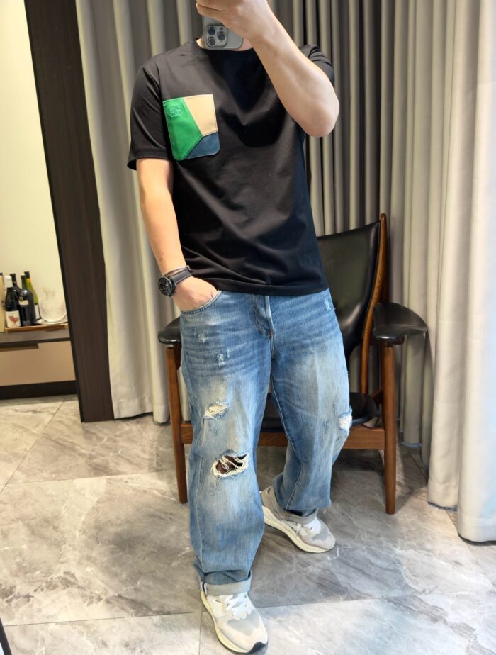 Persona in outfit casual con jeans scuciti, t-shirt con patch colorato e sneakers bianche.