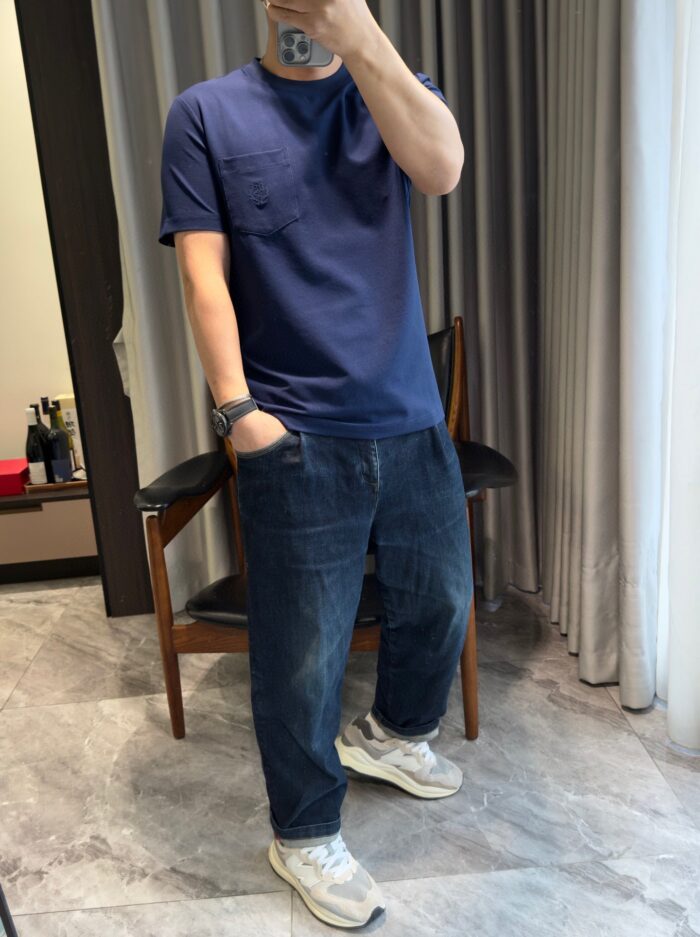 Persona in outfit casual: t-shirt navy, jeans medio, sneakers bianche, riflesso nel bagno luminoso.