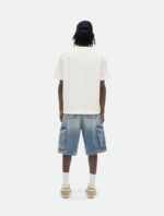 Abbigliamento casual estivo con shorts in denim, t-shirt oversize e scarpe slip-on beige.