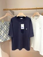 Abbigliamento estivo casual: T-shirt navy, bianca con logo e shorts a quadri su supporto in legno.