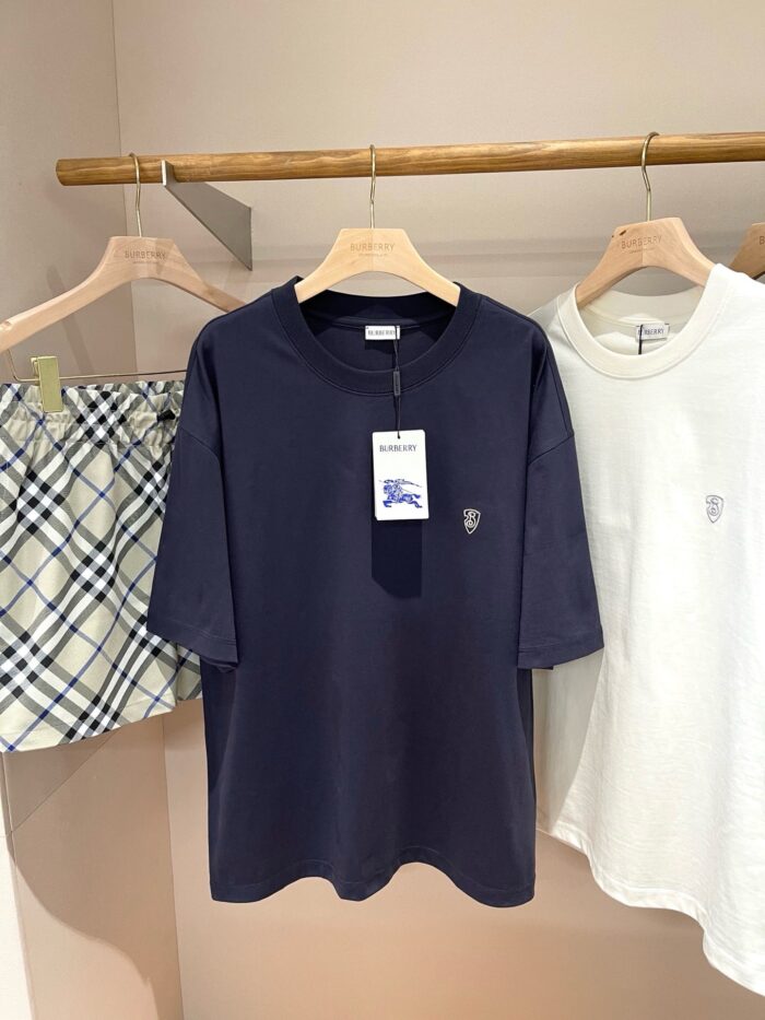 Abbigliamento estivo casual: T-shirt navy, bianca con logo e shorts a quadri su supporto in legno.
