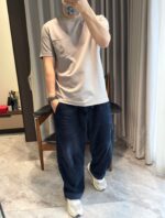 Outfit casual con t-shirt grigia, pantaloni blu larghi e sneakers bianche in ambiente moderno.