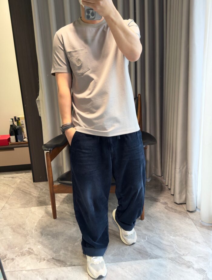Outfit casual con t-shirt grigia, pantaloni blu larghi e sneakers bianche in ambiente moderno.