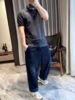 Uomo moderno in casual con pantaloni larghi, polo scuro e sneakers in ambiente elegante.