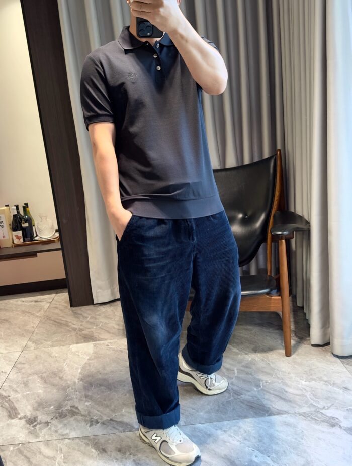 Uomo moderno in casual con pantaloni larghi, polo scuro e sneakers in ambiente elegante.