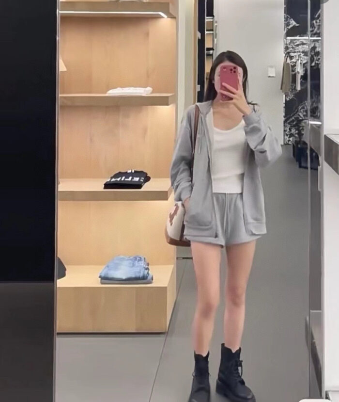Donna in negozio con outfit casual, hoodie grigia e stivaletti neri, riflesso nello specchio.