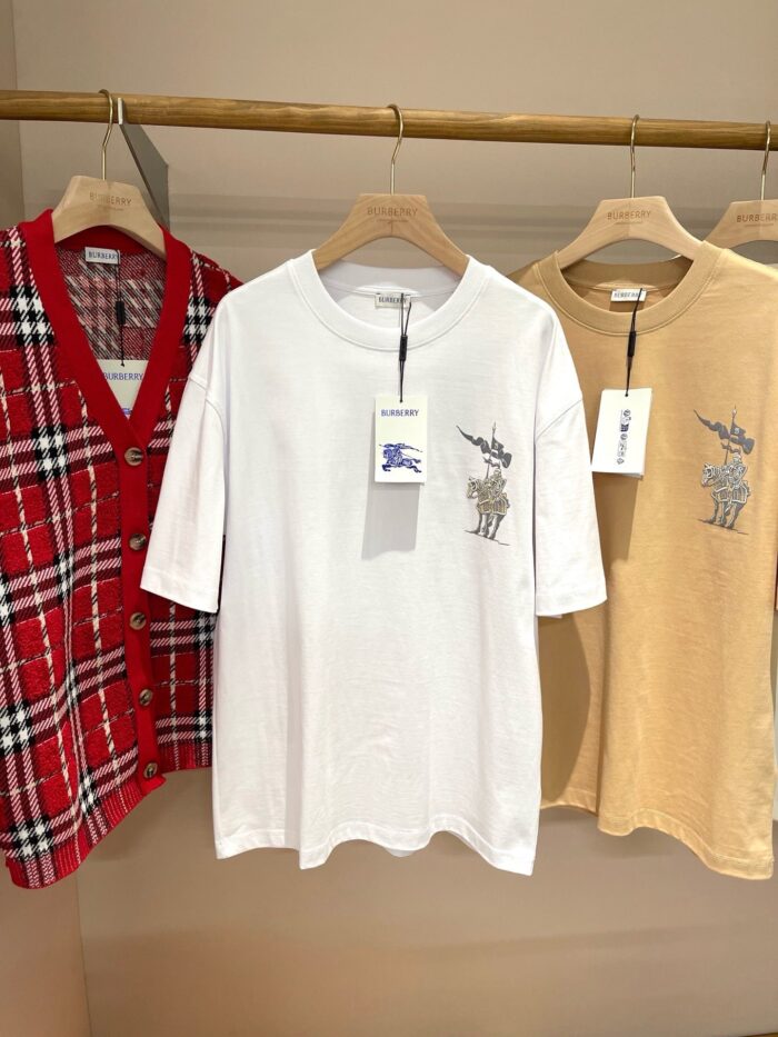 Abbigliamento casual: cardigan a quadri, T-shirt bianca e camicia beige su supporto in legno.