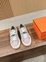 Sneakers rosa e grigio eleganti con scatola arancione su superficie di legno, stile minimalista.