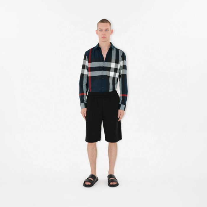 Modello con camicia a quadri, pantaloncini neri e sandali, stile casual estivo.