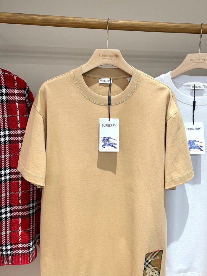 Esposizione di magliette casual beige, bianca e camicia a quadri rossa su appendini in legno.