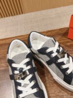 Sneakers casual in navy e grigio con fibbia decorativa e dettagli moderni, su superficie di legno.