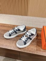 Sneaker casual in grigio e blu su superficie in legno con packaging arancione vibrante.