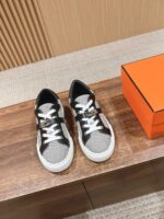 Sneakers eleganti grigio e nero con scatola arancione su superficie in legno.