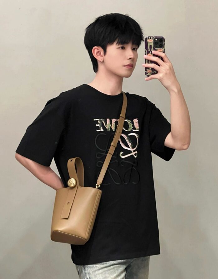 Giovane uomo in streetwear con t-shirt grafica, borsa tan e selfie, stile moderno e casual.