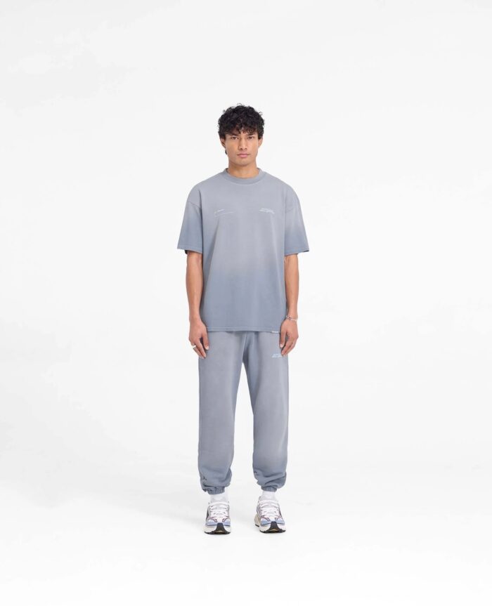 Uomo in streetwear grigio con sneakers bianche, stile casual e moderno in sfondo minimalista.