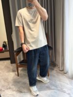 Giovane uomo casual con t-shirt beige e sneakers bianche in ambiente moderno e luminoso.