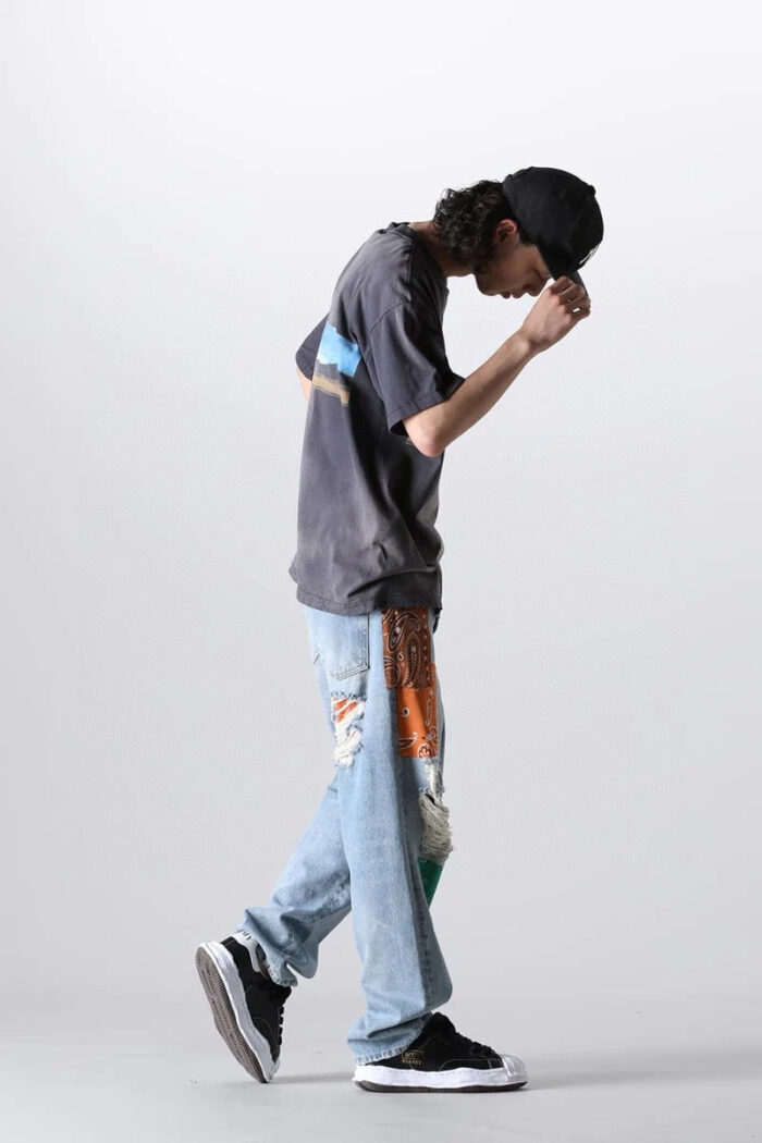 Giovane stile streetwear con jeans patchwork, t-shirt grafico, cappello nero e sneakers urbani.