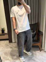 Persona in abbigliamento casual con jeans scuri, sneakers bianche e ambiente moderno interno.