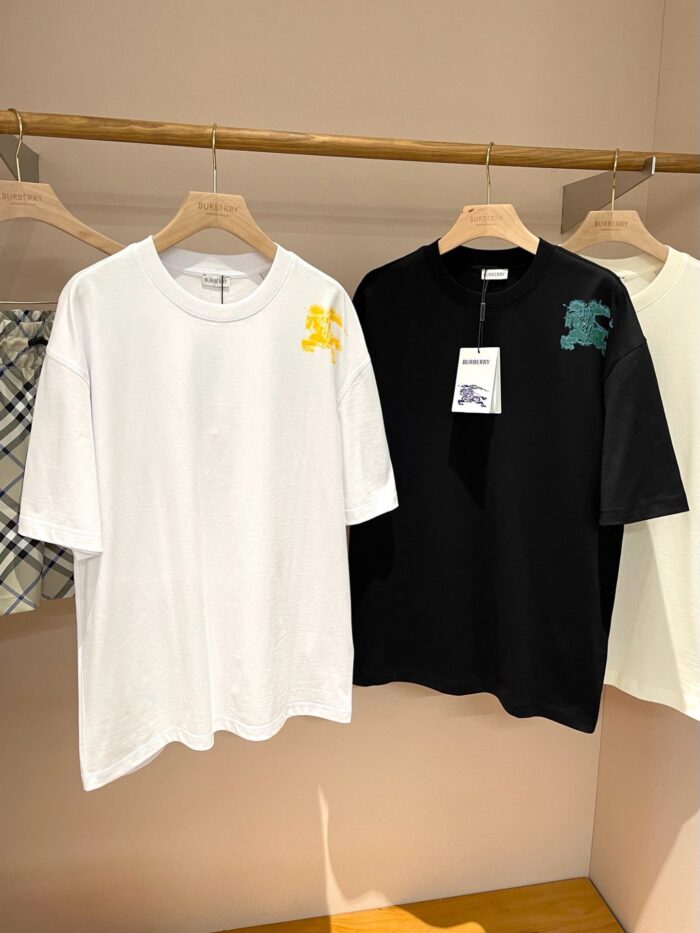 Magliette streetwear bianca e nera con grafiche colorate su supporto in legno, stile minimalista.
