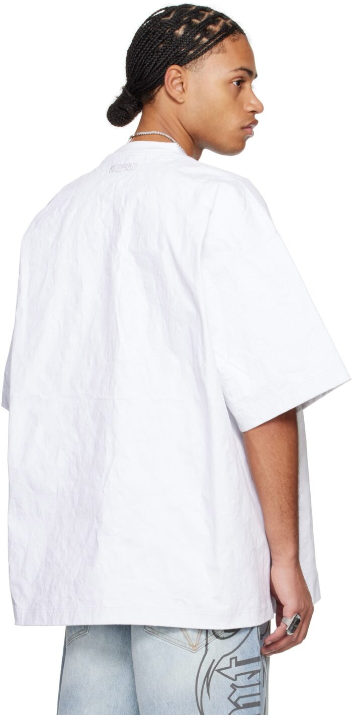 Giovane con capelli intrecciati, camicia oversize bianca e jeans destrutturati in stile streetwear.
