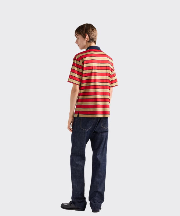 Uomo giovane con polo a righe rosse e gialle e jeans scuri, look casual e alla moda.