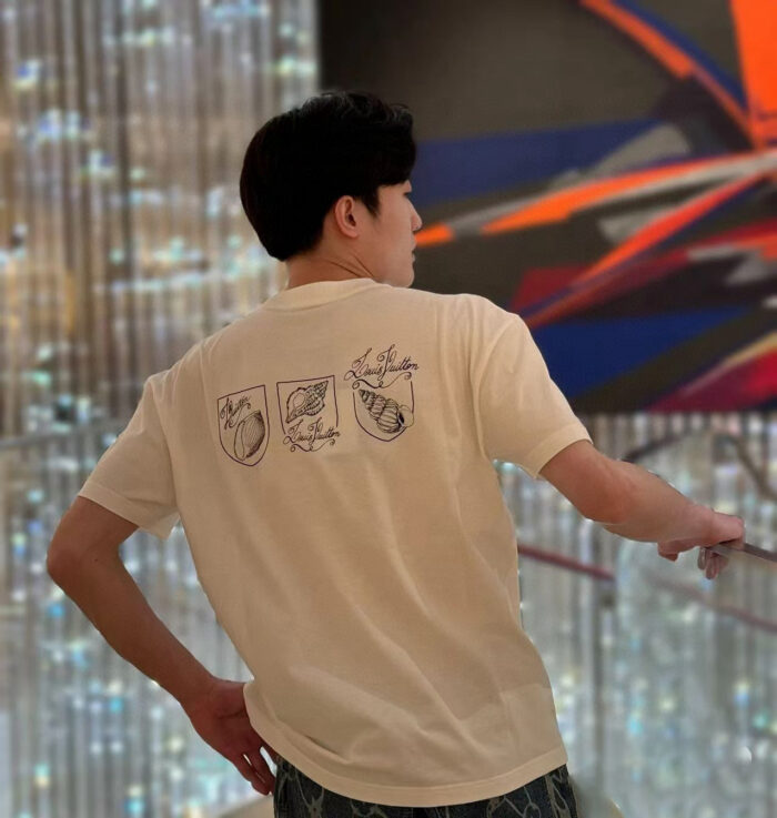 Uomo giovane indossa T-shirt con illustrazioni artistiche in ambientazione moderna e luminosa.