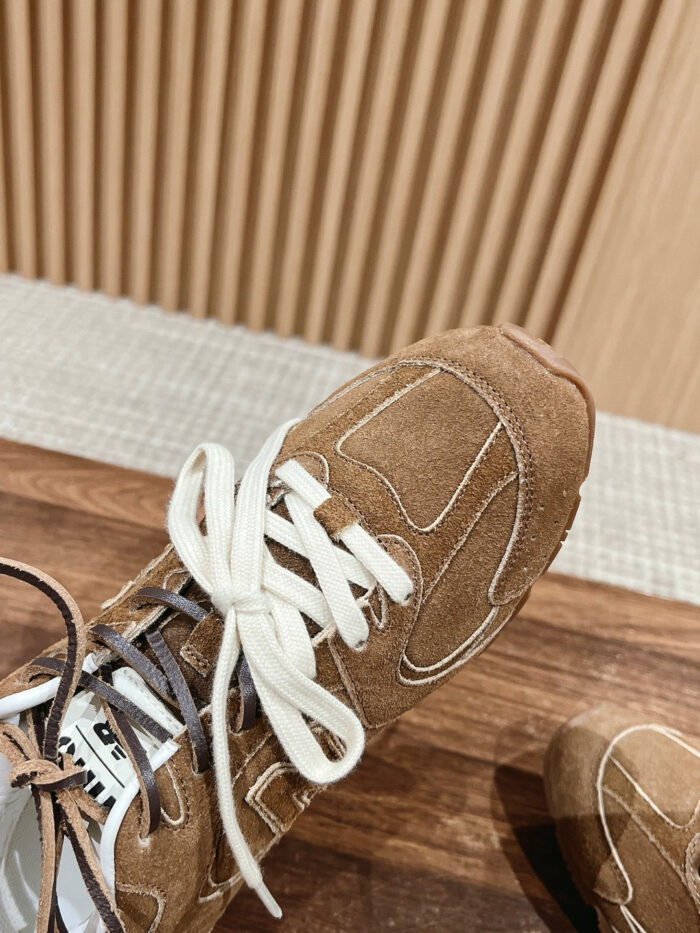 Sneakers in suede moka con lacci contrasti su pavimento in legno, stile casual e alla moda.