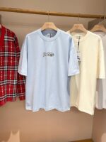 Lesposizione di tre t-shirt casual minimaliste: quadretti, azzurra con scritta, bianca elegante.