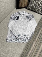 Camicia bianca elegante con motivi floreali su divano decorato, stile casual e raffinato.
