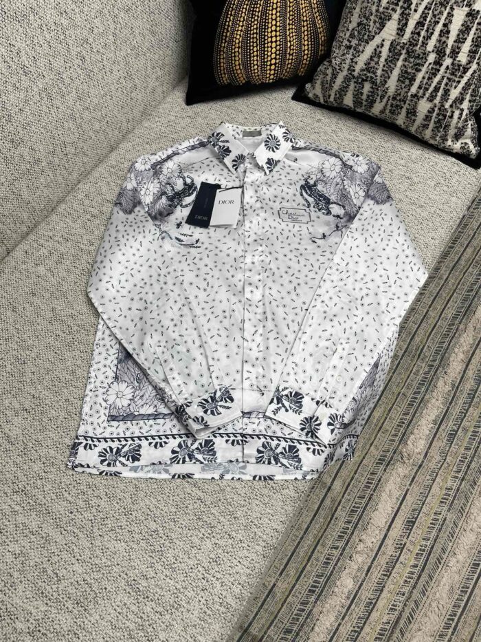Camicia bianca elegante con motivi floreali su divano decorato, stile casual e raffinato.