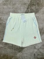 Pantaloncini bianchi casual con coulisse, tasche e dettagli blu, logo rosso sul lato.