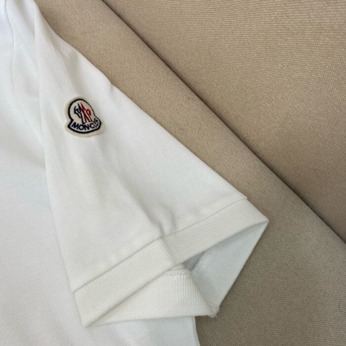 T-shirt bianca casual con ricamo, maniche arrotolate su sfondo beige, stile semplice e di qualità.