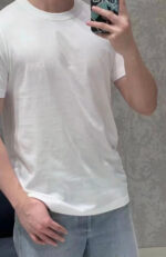 Ragazzo sorride in camerino con T-shirt bianca e jeans chiari, stile casual moderno.