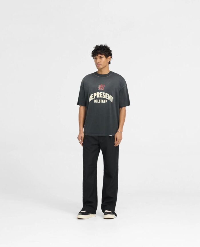 Giovane uomo con maglietta grafica, pantaloni neri e capelli ricci in stile casual moderno.