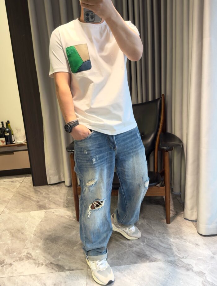 Uomo giovane in stile casual con jeans distressed e sneakers bianche in ambiente elegante.