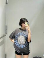 Donna giovane in cabina prova con t-shirt oversize grigia e shorts neri, selfie alla moda.