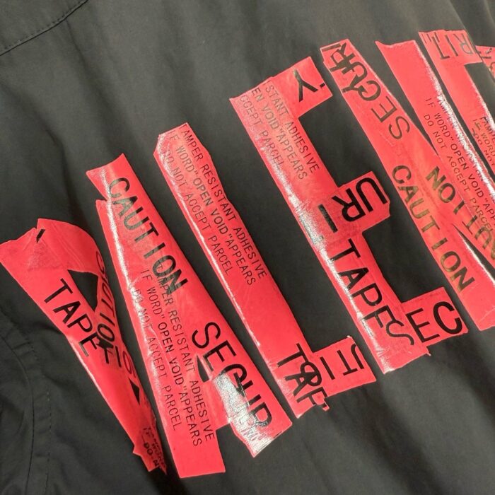 Abbigliamento contemporaneo con tape rosso caution su sfondo nero, stile urbano e artistico.