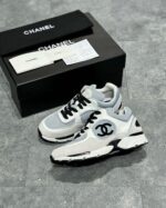 Sneaker Chanel di lusso in grigio e bianco con logo iconico e dettagli in pelle e suede.