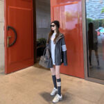 Donna giovane in stile urbano chic davanti a porte rosse moderne.